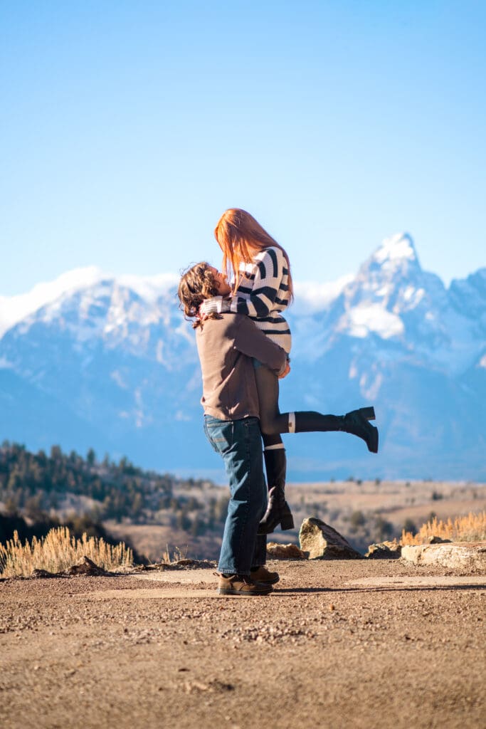 Man lifting woman in front of view of the Grand Tetons.