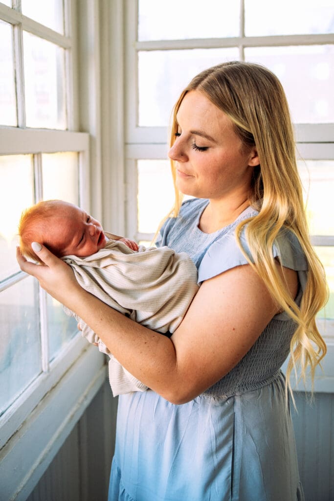 Woman cradling newborn in left arm on an enclosed porch.
