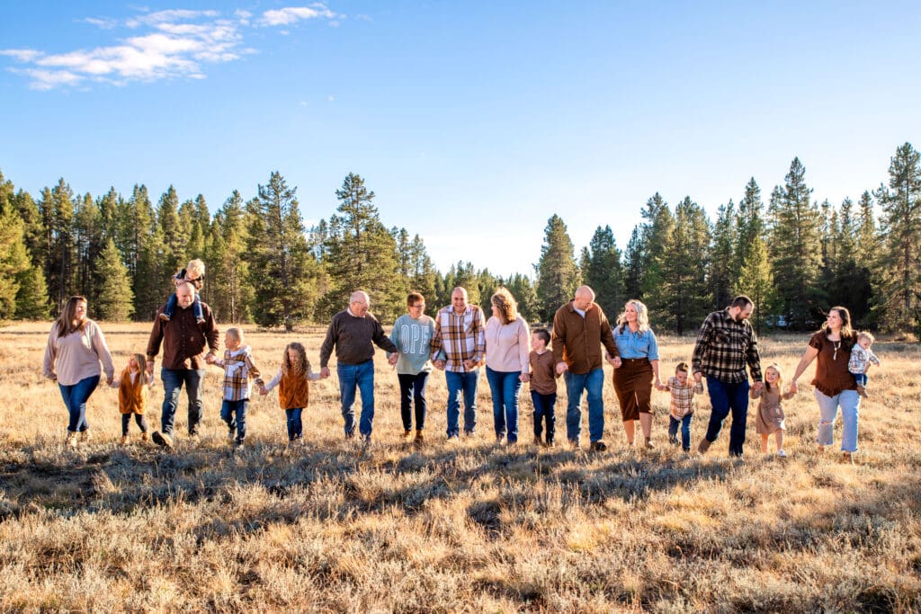 Extended family holding hands and walking through fields while talking and laughing with each other.