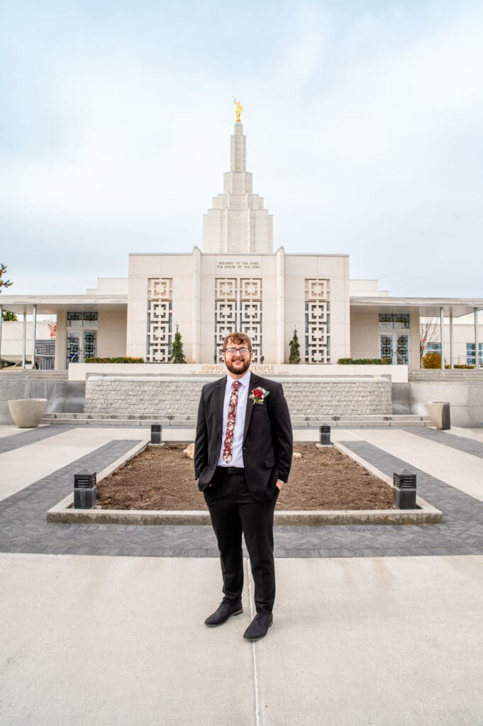 Groom smiling at camera with hands in pockets with beautiful blue skies and Idaho Falls Temple in the background.