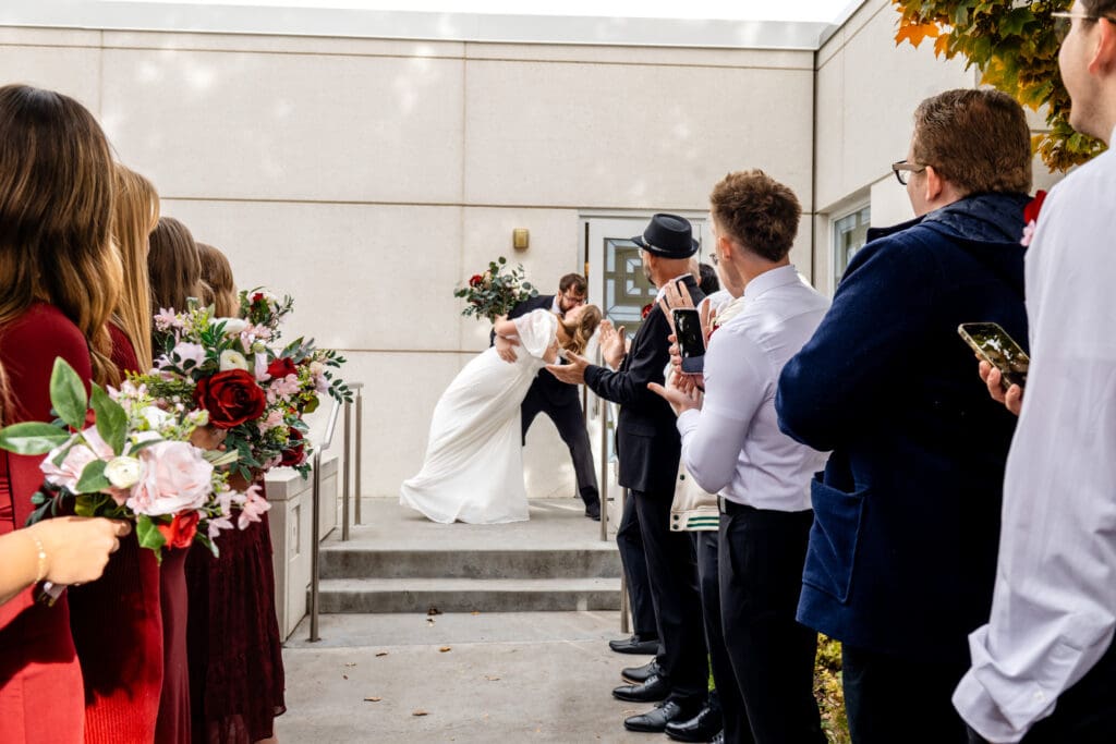 Groom dip and kissing bride on the steps of the Idaho Falls Temple bridal exit with friends and family watching.