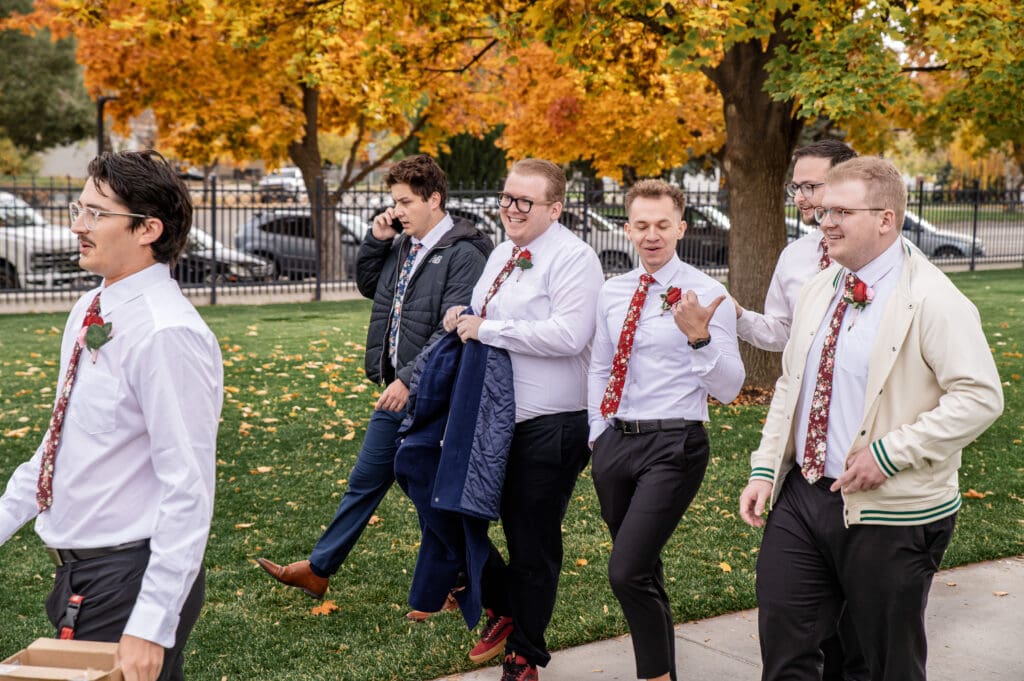 Groomsmen walking, smiling, and talking on the sidewalk of Idaho Falls Temple as they move to take group photos.