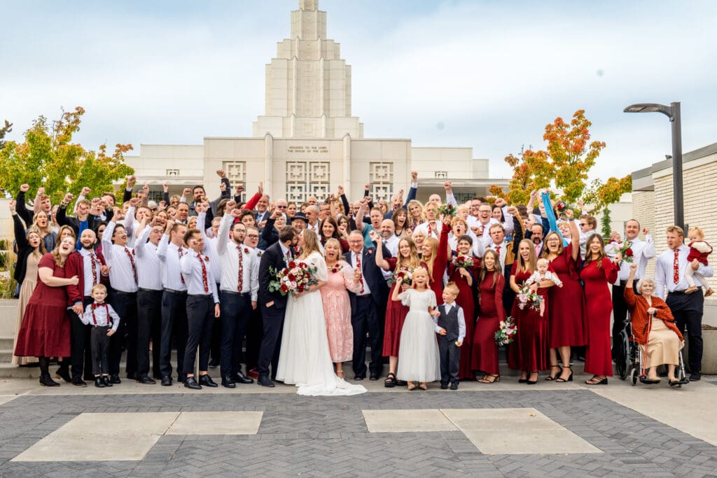 Big group of family and friends cheer as bride and groom kiss with beautiful blue skies and the Idaho Falls Temple behind them.