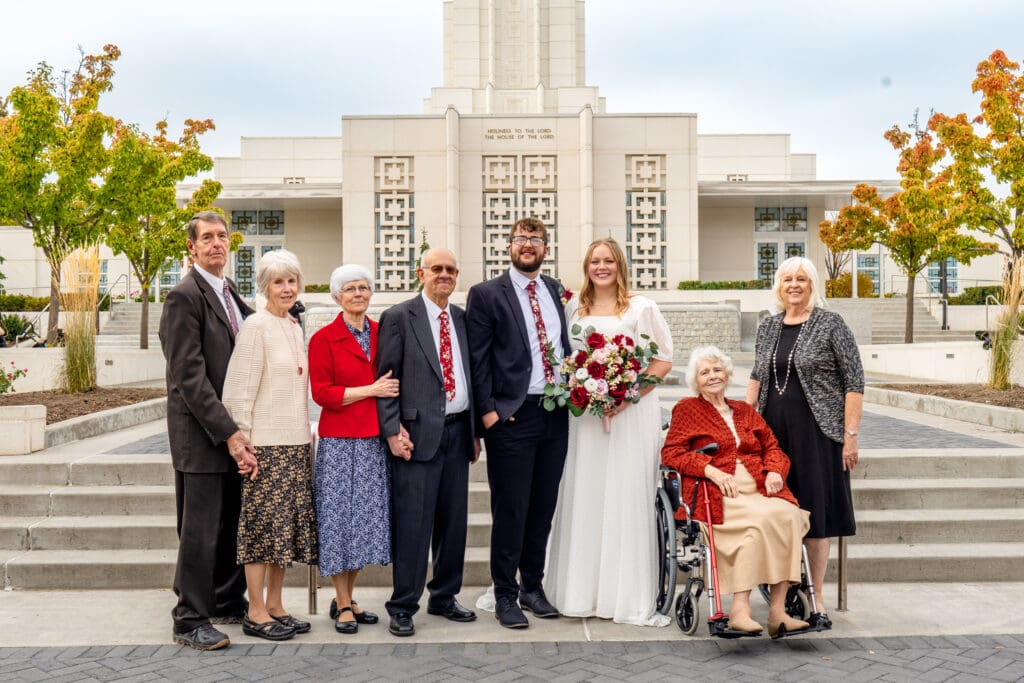 Small group of grandparents pose with bride and groom and smile at camera with beautiful blue skies and the Idaho Falls Temple behind them.