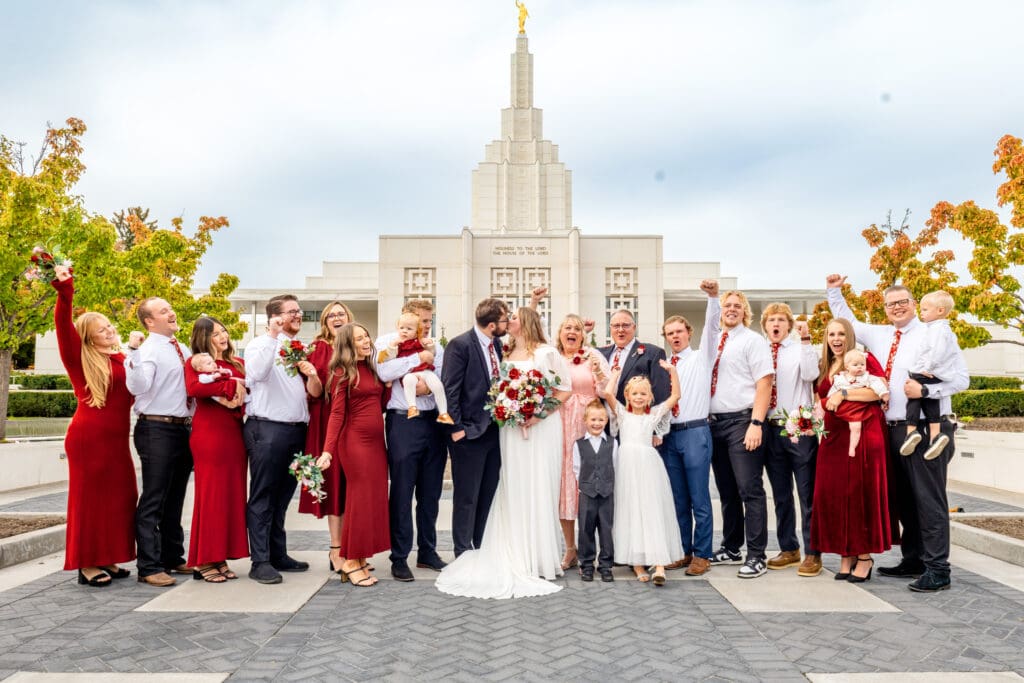 Small group of family and friends cheer as bride and groomkiss with beautiful blue skies and the Idaho Falls Temple behind them.