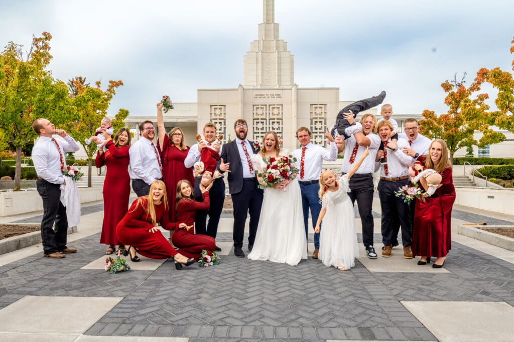Small group of family and friends make silly poses with bride and groom with beautiful blue skies and the Idaho Falls Temple behind them.