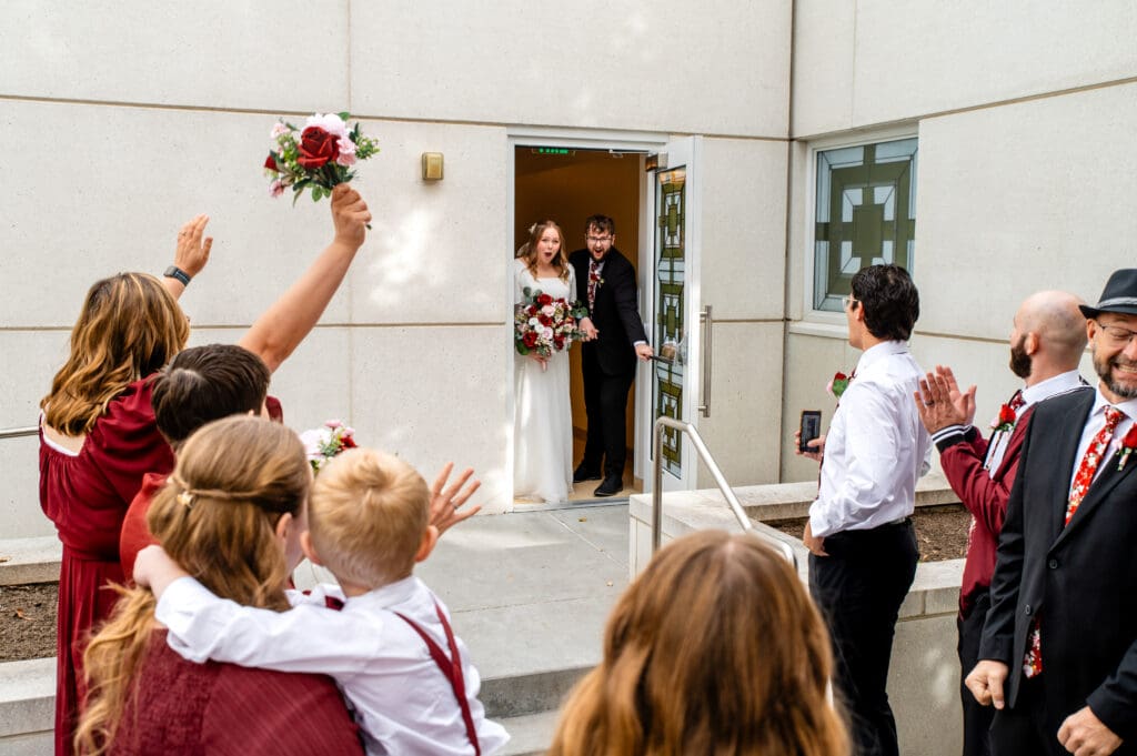 Groom opening door as the wedding couple exits the Idaho Falls temple and friends and family cheer.