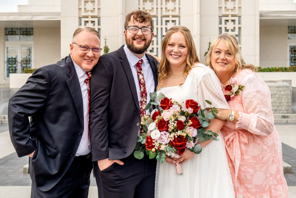 Small group of parents pose with bride and groom and smile at camera with the Idaho Falls Temple behind them.