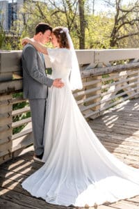 Bride and groom facing each other, touching foreheads, and leaning against bridge rail as bride wraps her arms around groom's neck and groom holds her hip on bridge in Idaho Falls.