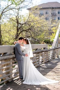 Bride and groom facing each other, touching foreheads, and leaning against bridge rail as bride wraps her arms around groom's neck and groom holds her hip on bridge with city building background in Idaho Falls.