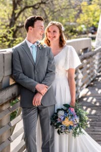 Bride and groom smiling at each other as they lean against bride rail while bride holds bouquet at her left side in Idaho Falls.