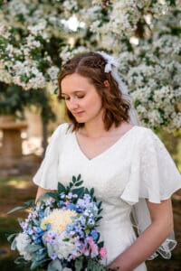 Bride looking down at colorful spring bouquet in front of tree blossoms in Idaho Falls.