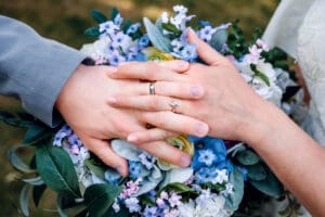 Bride and groom's wedding rings on their fingers with their hands interlaced and resting on top of colorful spring bouquet in Idaho Falls.