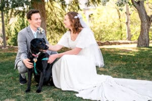 Bride and groom smiling at each other and kneeling as they pet their dog in Idaho Falls.