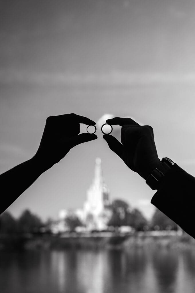 Bride and groom's hands holding rings to sky with Idaho Falls Temple and Snake River in the background in black and white.