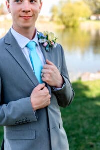 Blue tie, colorful spring boutonniere, and groom's hands holding suit collar in Idaho Falls.