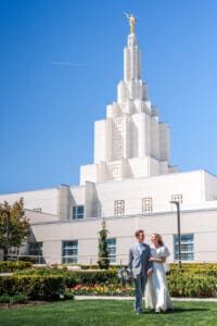 Bride holding groom's arm and groom holding bouquet as they walk across the grass in front of the Idaho Falls temple.