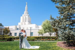 Bride and groom facing each other, touching foreheads, and holding bouquet at waist level in front of Idaho Falls Temple.