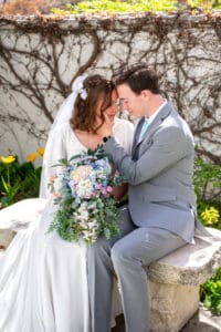 Bride and groom sitting on bench under blossoms as they smile and touch foreheads with closed eyes with groom's hand holding bride's cheek and bouquet sits on their laps at Idaho Falls temple.