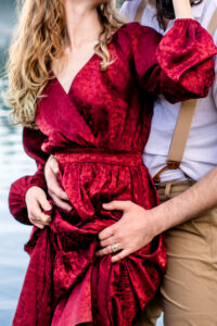 Man and woman in red dress hold and scrunch the skirt of her dress while showing off jewelry, captured by Utah engagement photographer.