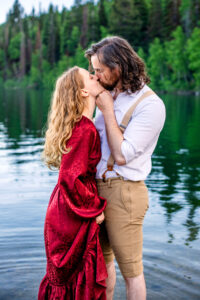Man places hand on woman's jaw as woman holds skirt of dress and they kiss while standing in lake, captured by Utah engagement photographer.
