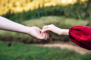 Man and woman with red dress sleeve curve and hold hands to make an s, showcasing engagement rings, captured by Utah engagement photographer.