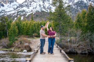 Man holds woman's hands and spins her on bridge over river with mountains in back, captured by Grand Teton Engagement photographer.