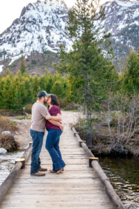 Man holds brings woman in for a kiss on bridge over river with mountains in back, captured by Grand Teton Engagement photographer.