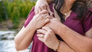 Woman's jewelery as man wraps arms around wife and she hold his hands, captured by Grand Teton Engagement Photographer
