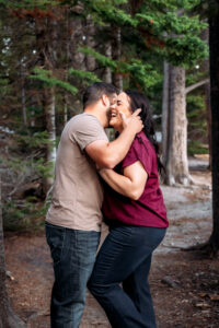 Woman laughing and leaning into man who is brushing hair out of her face on trail, captured by Grand Teton engagement photographer.