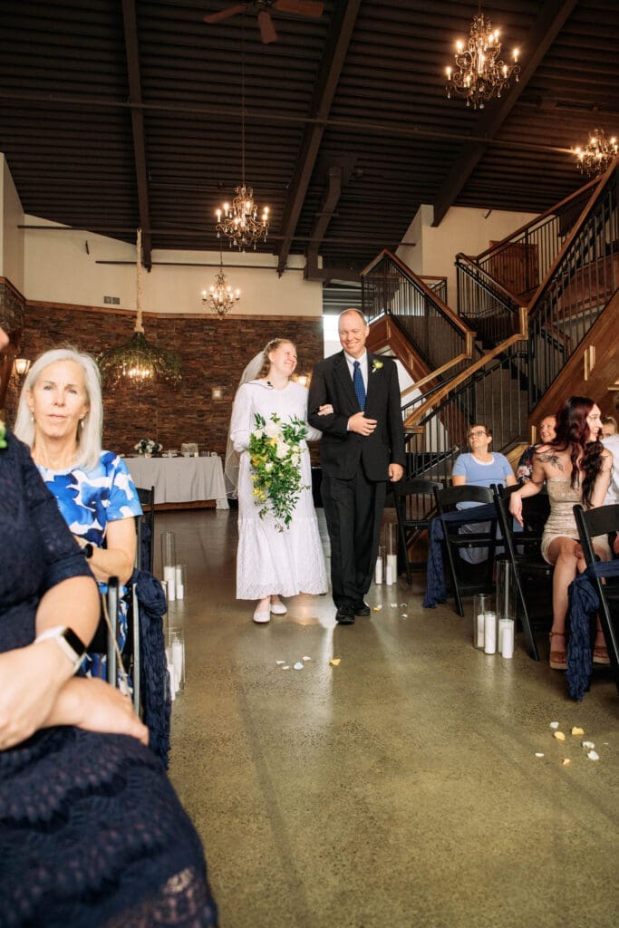 Round guest entrance table with white linen in front of dark wooded diamond arch with greenery at The Atrium, captured by Rexburg wedding photographer.
